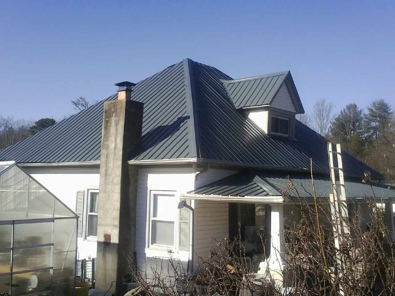 Dark blue standing seam metal roof on a white farmhouse with dormer — Slate & Tile Roof Repair by Roofing Brothers in Basco