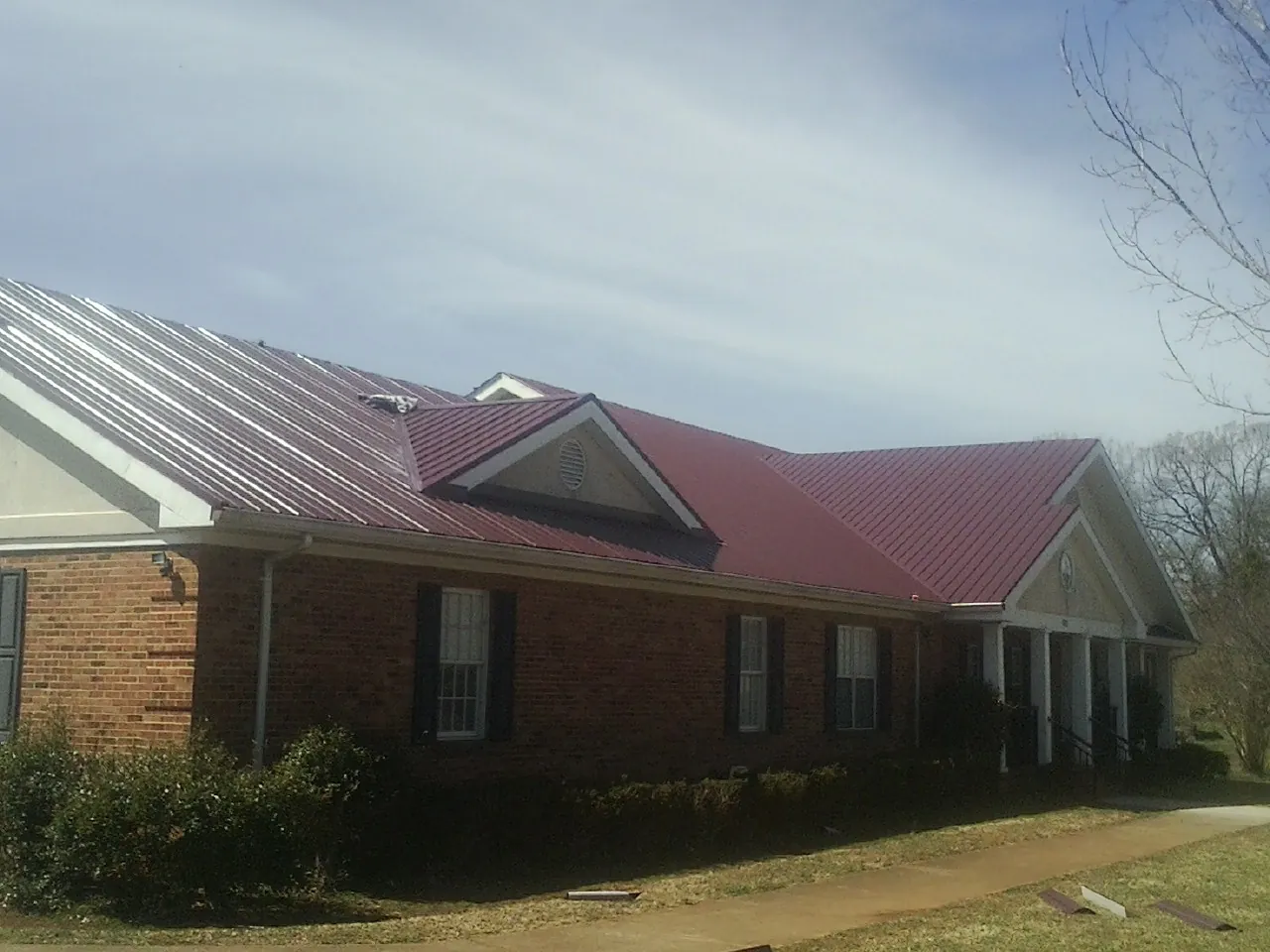 Red metal roof with gabled entries on a long brick building, from a Hail Damage Roof Repair job in Basco