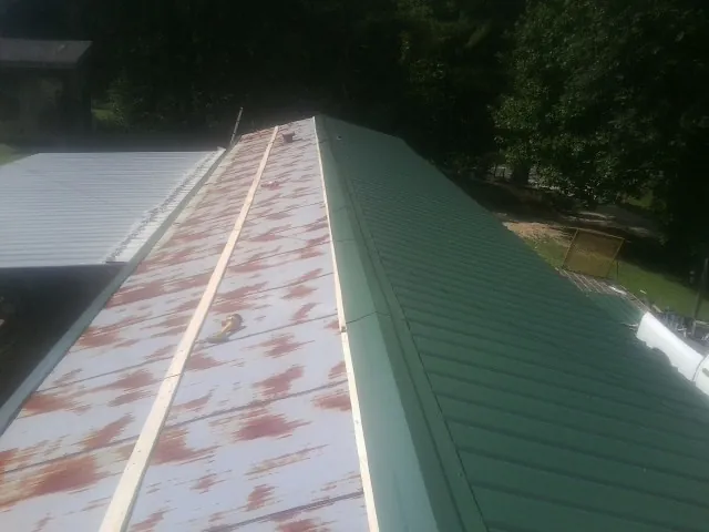 Old rusted panels beside newly installed green metal roofing — Wind Damage Roof Repair by Roofing Brothers in Basco