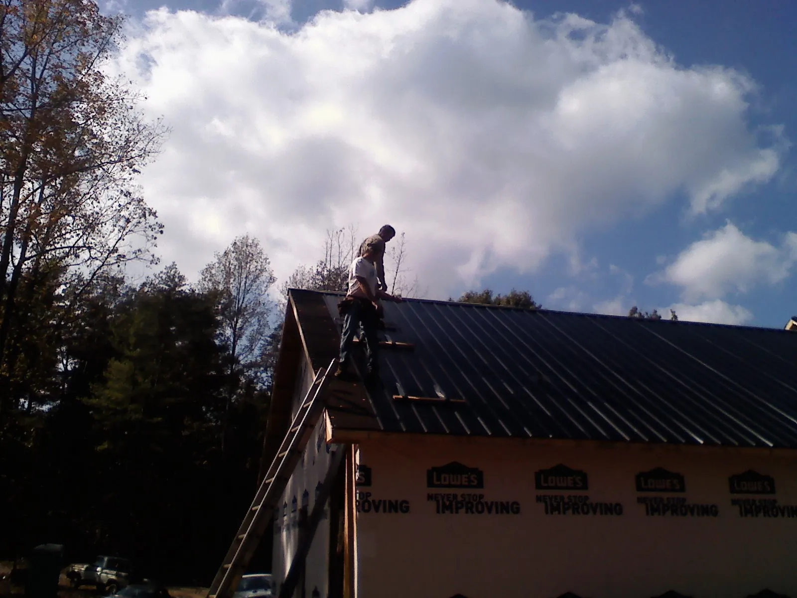 Roofer fastening dark metal panels high against a cloudy sky, from a Roof Inspection job in Basco