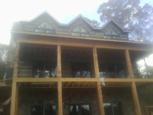 Dormers and porch framing on a large log home under construction — Roof Coating work by our crew in Basco
